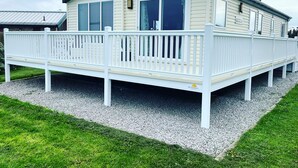 A mobile home with a white deck, a solar panel on the roof, and a gravel driveway. - Beautiful Lodge w/Amazing Coastal Views (Hartlepool)