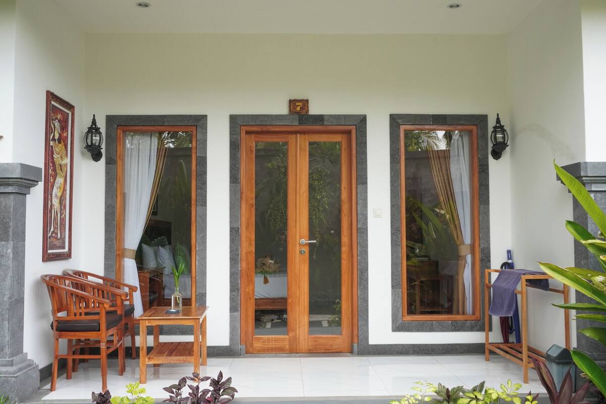 Un porche cubierto con una mesa y sillas de madera, una puerta de cristal y un pequeño banco de madera.