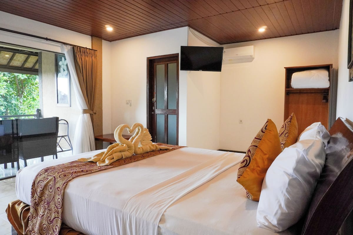 Habitación de hotel con cama, televisor montado en la pared, puerta de madera y ventana con cortinas.