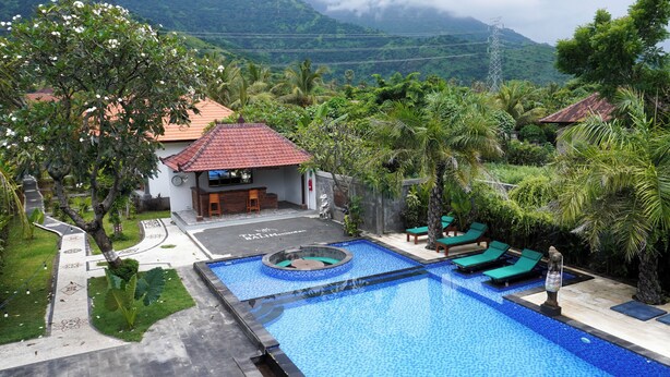 A swimming pool with a circular hot tub, surrounded by lounge chairs and palm trees, with a mountain backdrop. - Bali Menjangan Boutique Villas (Pemuteran)