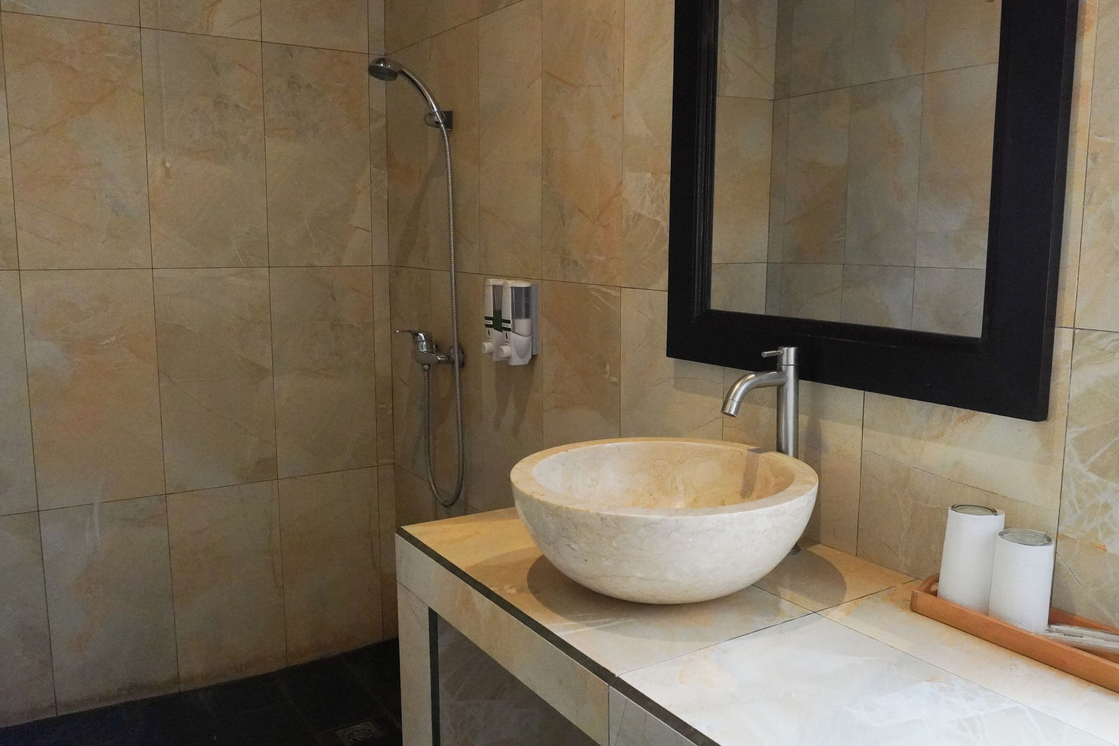 A bathroom with a large, round, beige sink, a mirror, and a shower area.