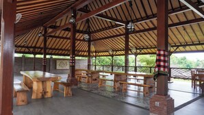 An open-air pavilion with wooden benches and tables, a brick column, and hanging lights. - Bali Menjangan Boutique Villas (Pemuteran)