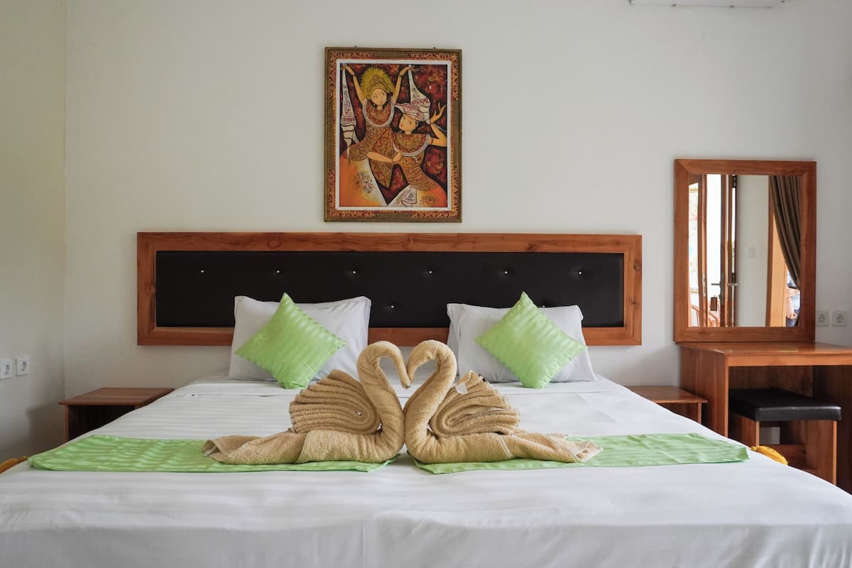 Habitación de hotel con una cama grande, dos almohadas verdes, un cabecero de madera, un cuadro en la pared y un espejo a la derecha.