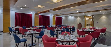A hotel dining area with tables and chairs, red and blue chairs, and a marble floor.