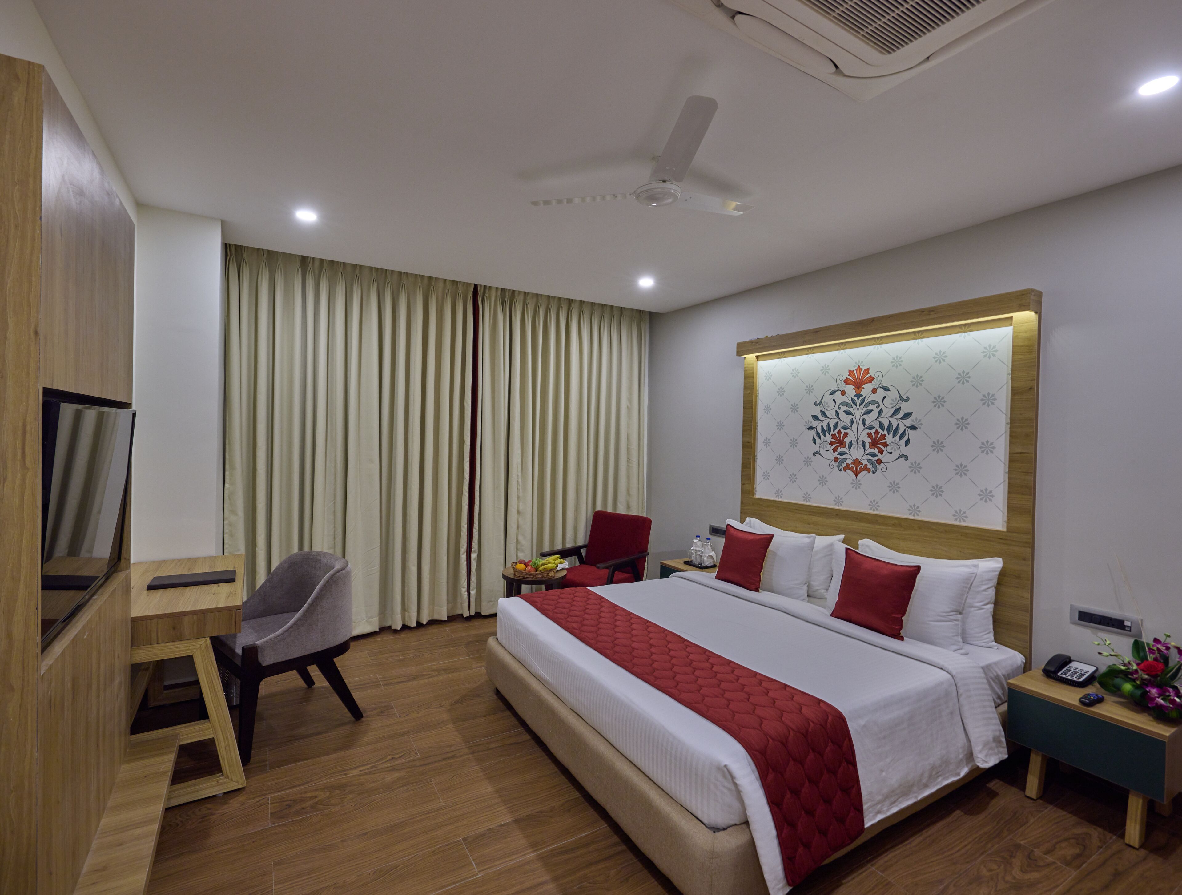 A hotel room with a bed, a desk, a chair, a nightstand, and a wall-mounted artwork.