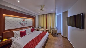 A hotel room with a large bed, a ceiling fan, a TV, a small table, and a chair. - Golden Tulip Tirupati (Tirupati)