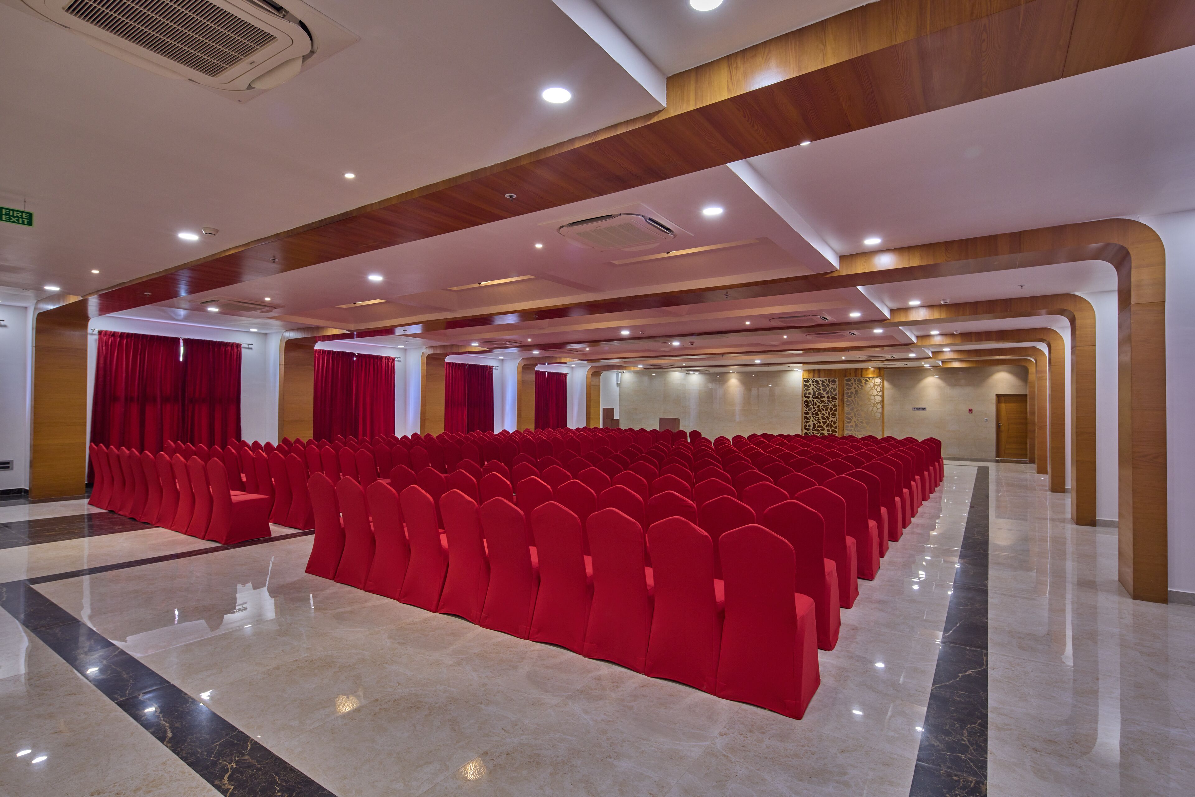 A conference room with rows of red chairs, wooden paneling on the ceiling, and a polished marble floor.