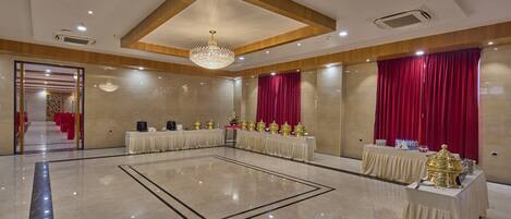 Un amplio salón con piso de mármol pulido, una araña central y mesas dispuestas para un evento formal.