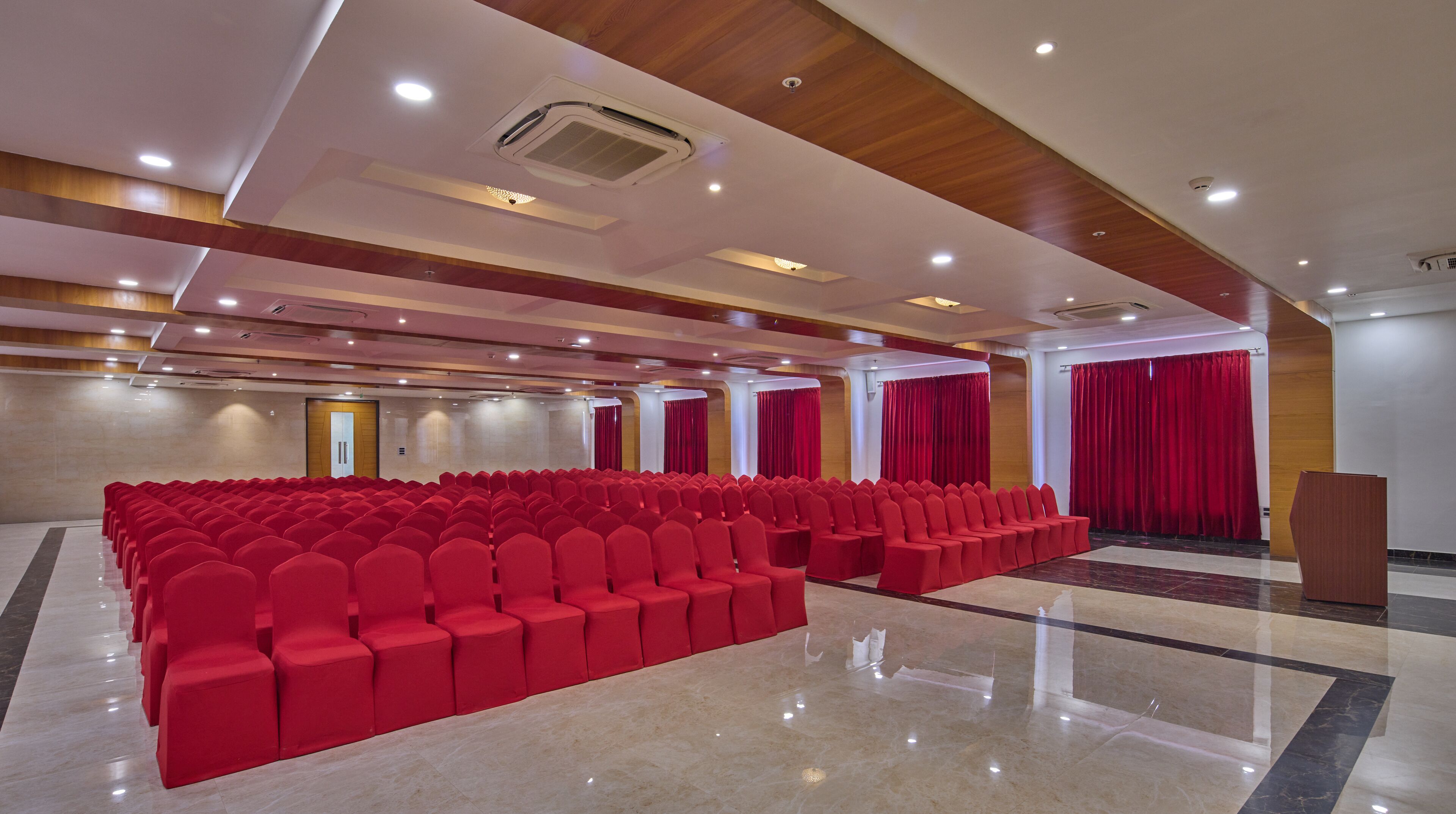 Una sala conferenze con file di sedie rosse, un podio e tende rosse.