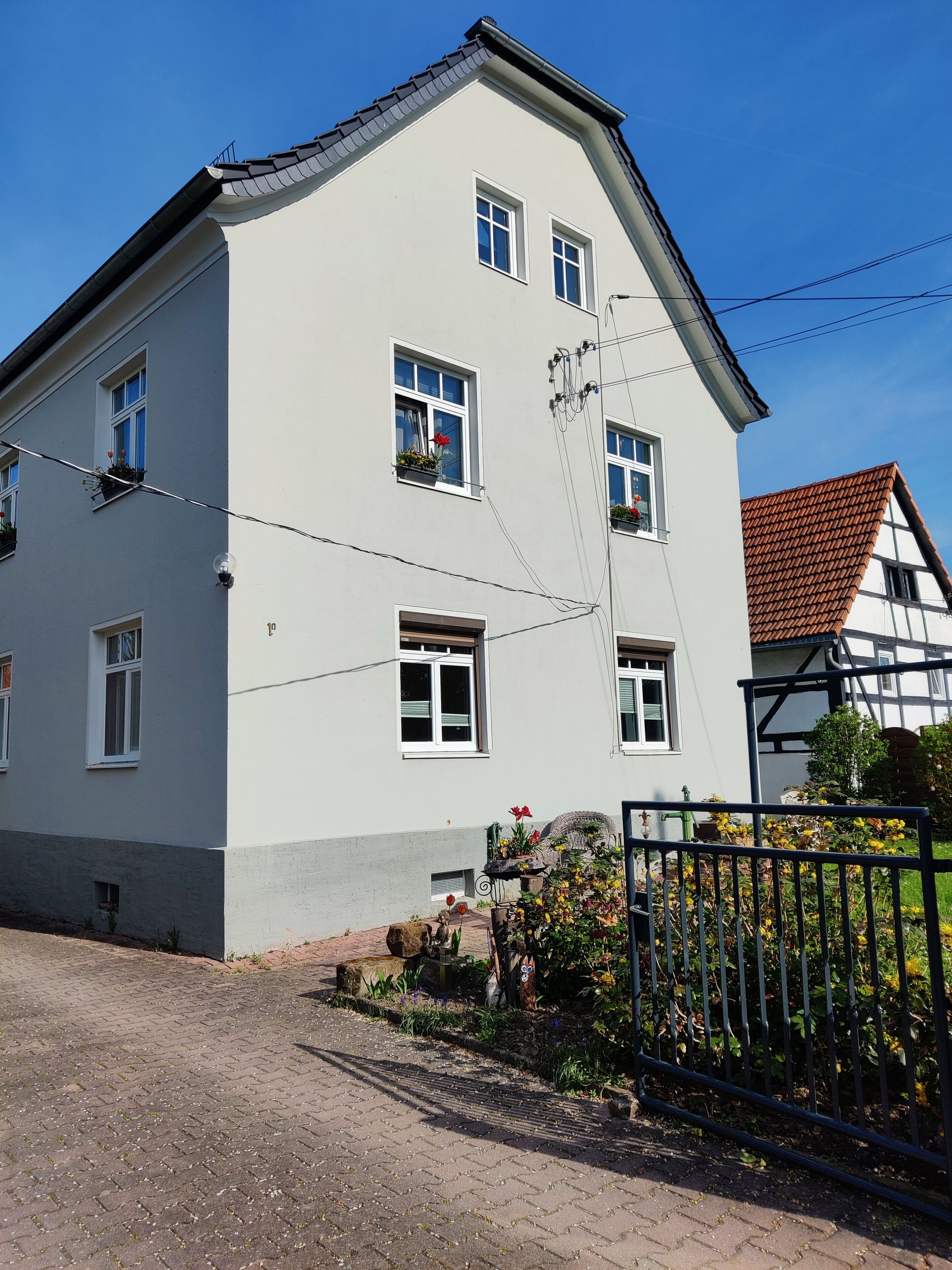 Ein zweistöckiges Gebäude mit zahlreichen Fenstern, einer sichtbaren Tür und einem kleinen Garten mit Blumen und Pflanzen.