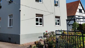 Un bâtiment à deux étages, doté de nombreuses fenêtres, d’une porte bien visible et d’un petit jardin agrémenté de fleurs et de plantes.