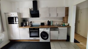 Une cuisine compacte avec des meubles blancs, un four encastré, un lave-vaisselle, une machine à laver et un four à micro-ondes.