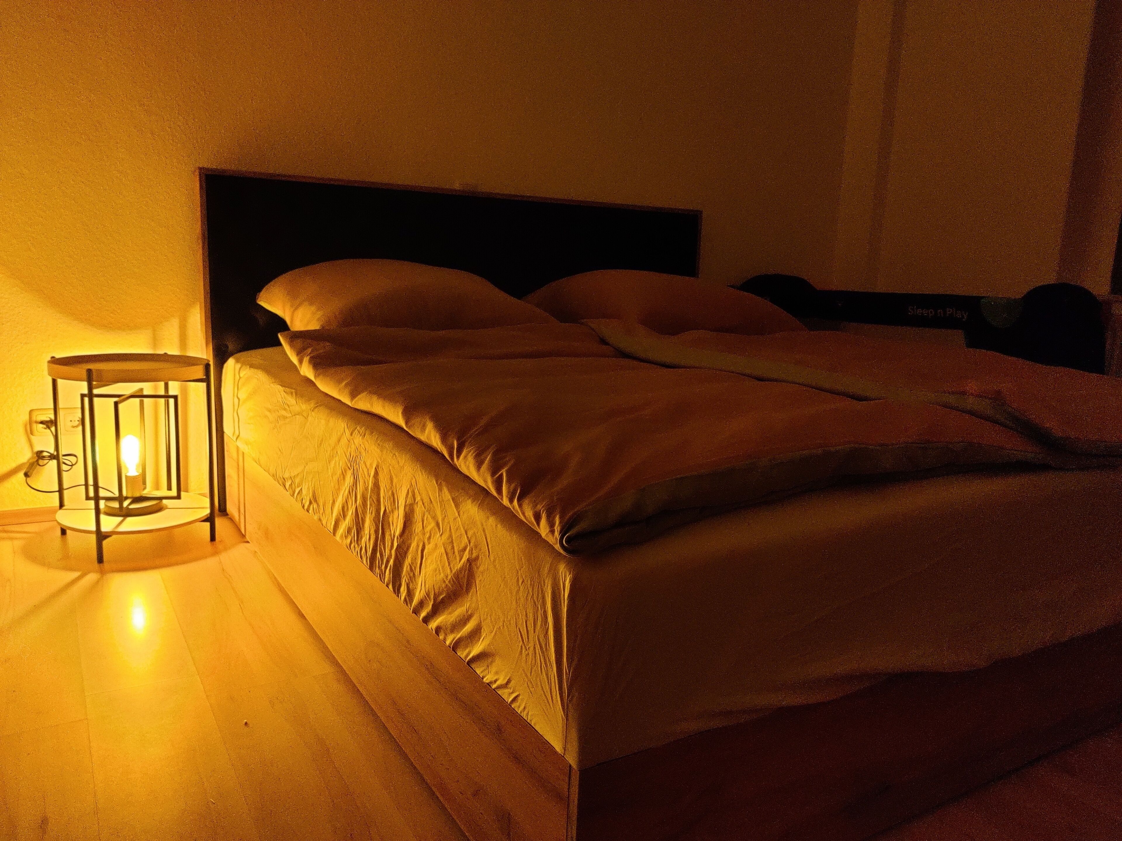 A bed with a headboard, a bedside table with a lamp, and a wall socket.