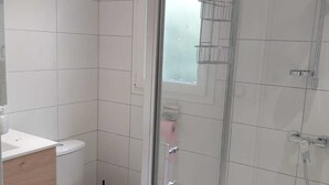 A modern bathroom with a glass shower enclosure, a white toilet, and a wooden vanity.