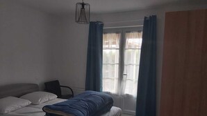 A bedroom with a bed, a chair, a window with curtains, and a hanging light fixture.