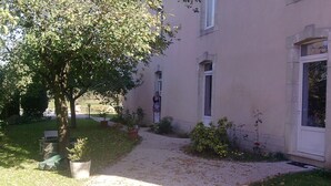 A building with a paved pathway leading to a door, surrounded by greenery and potted plants. - Les Pieds dans l'eau with swimming pool and Meuse riverfront (Belleray)