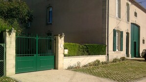 A gated entrance with a paved driveway leading to a building with a beige facade and green shutters. - Les Pieds dans l'eau with swimming pool and Meuse riverfront (Belleray)