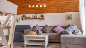 Een woonkamer met een grijze bank, een witte salontafel en een houten plafond.