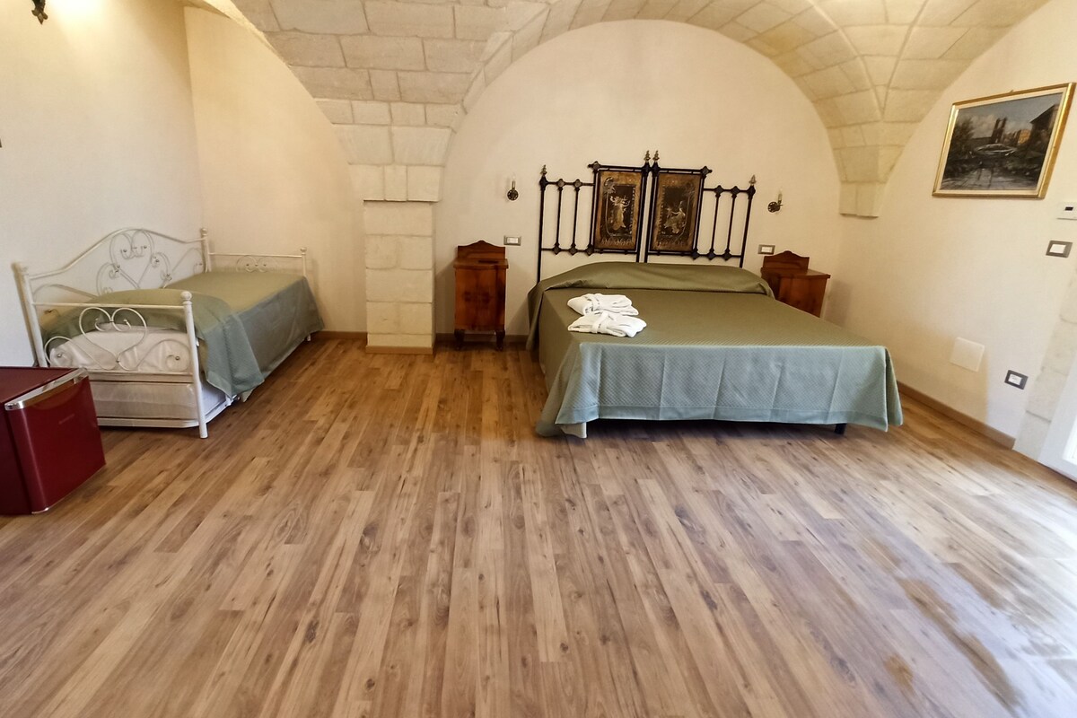Une chambre avec deux lits, un plancher en bois, une petite armoire rouge et un mur en pierre.