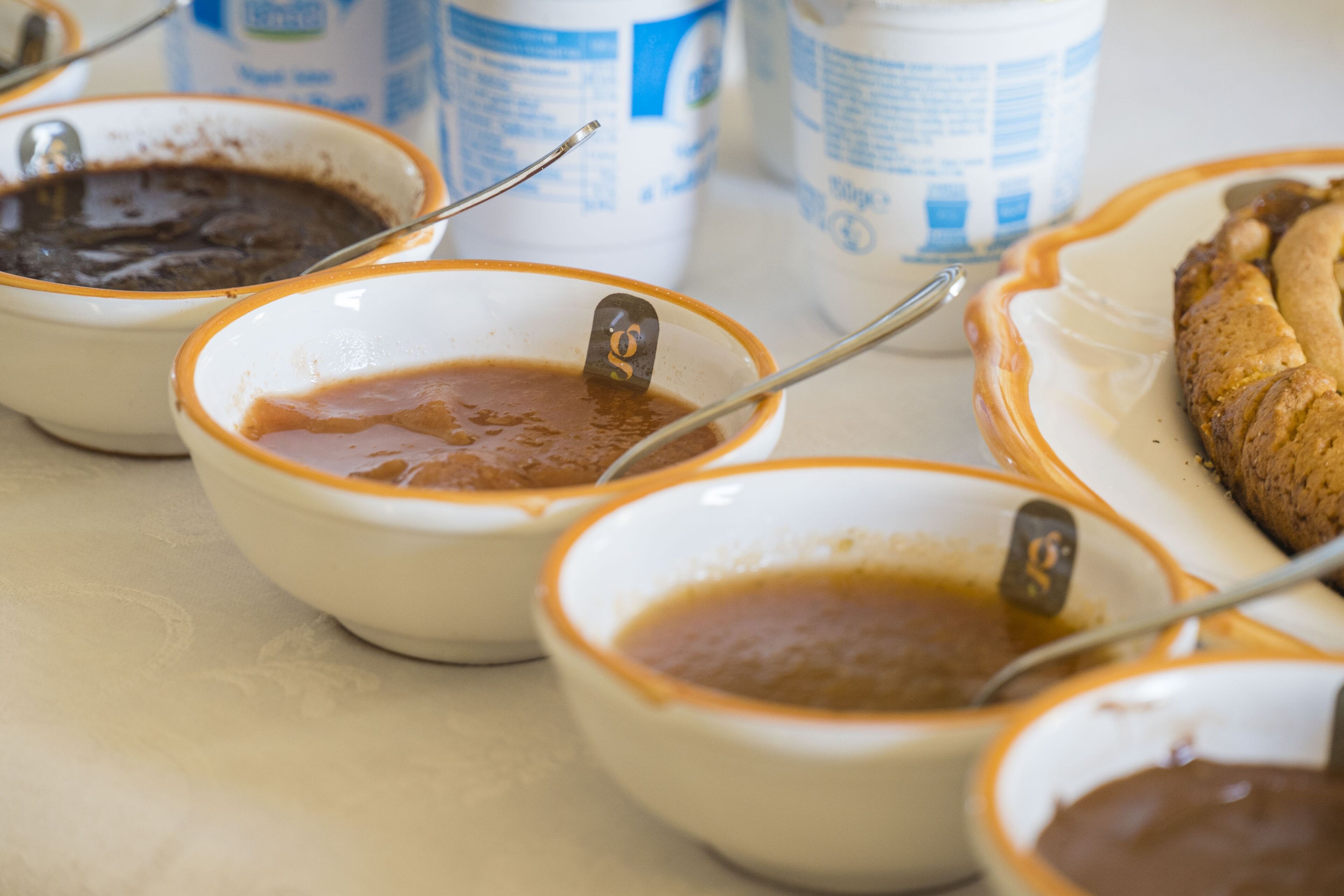 Varios recipientes de salsas con cucharas, un plato con un pastel y algunos envases al fondo.