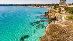 Un paysage côtier caractérisé par une eau turquoise cristalline, des falaises rocheuses et une structure en pierre d’importance historique.