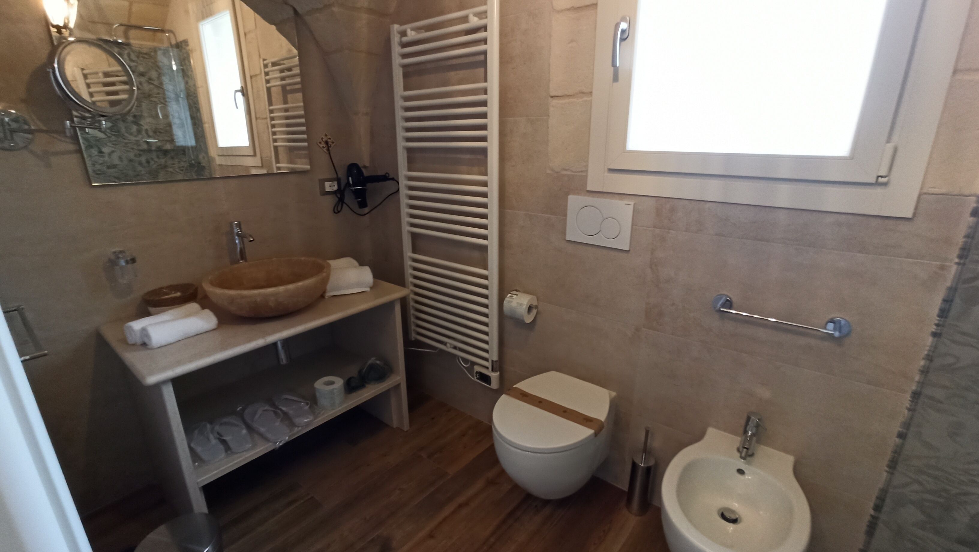 Un baño con tocador de madera, inodoro, bidé, lavamanos y ventana.