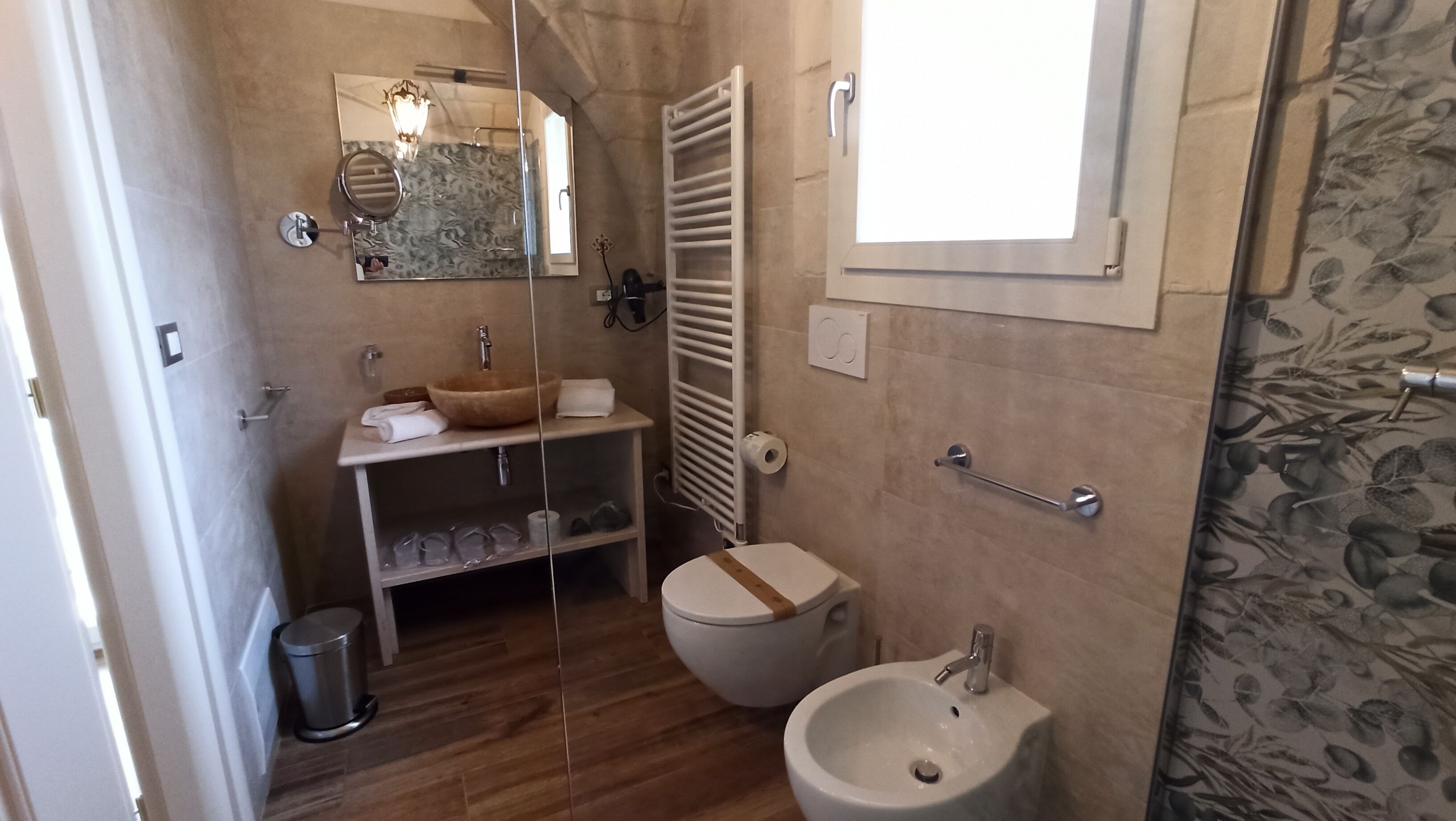 Ein Badezimmer mit einem Holzkosmetikschrank, einem großen Spiegel, einer Toilette, einem Bidet und einem Waschbecken.