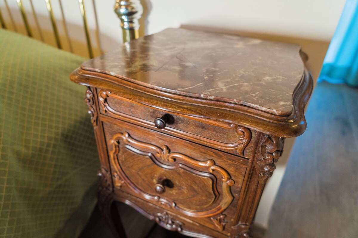 A wooden nightstand with a drawer and a small cabinet, placed next to a bed with a green bedspread.