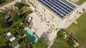 Eine Vogelperspektive eines Gebäudes mit einer Solaranlage auf dem Dach, einem Schwimmbad und umliegender Bepflanzung.