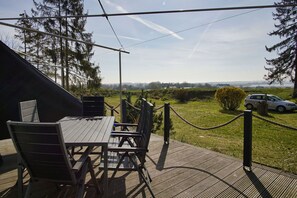 An outdoor deck with a table and chairs, overlooking a grassy area with a car and trees. - Ferienwohnungen auf dem Teschenberg Wohnung 01 (Middelhagen)