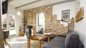 Una sala de estar moderna con una pared de ladrillo, una mesa de centro de madera, un sofá gris y una lámpara de pie negra.