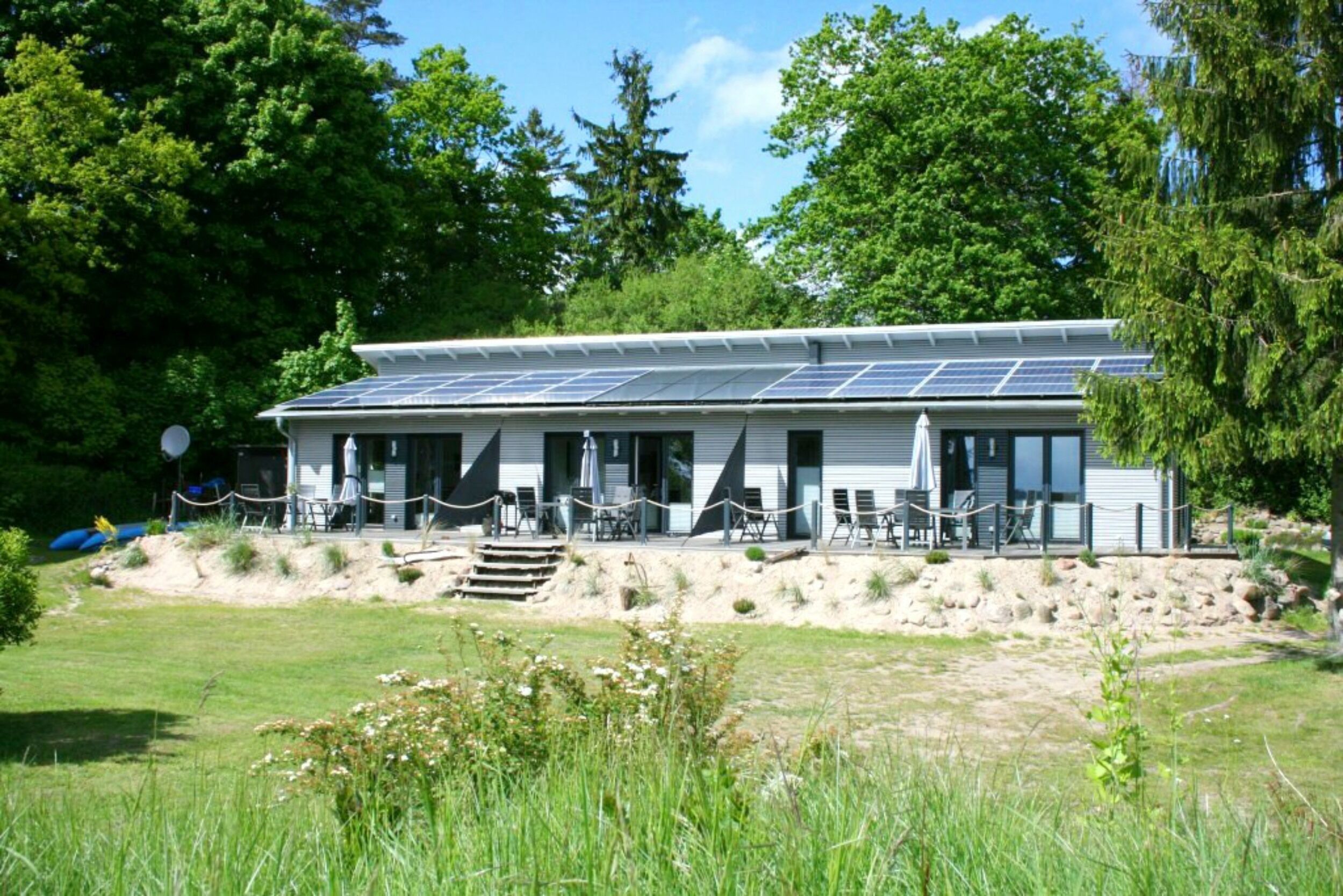 A building with solar panels on the roof, a covered outdoor seating area, and a natural setting with trees and grass.