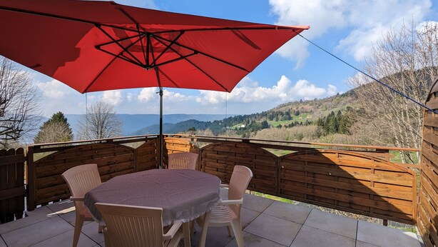 A patio with a table and chairs under a red umbrella, overlooking a scenic landscape. - Converted chapel into independent cottage with terrace and fireplace (Saulxures-sur-Moselotte)