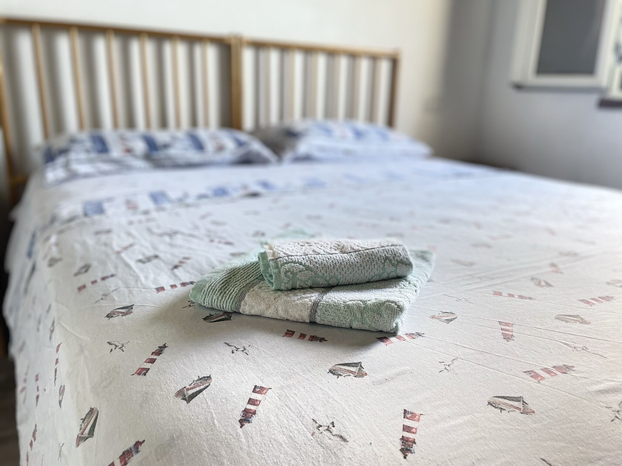 A neatly made bed with a patterned bedspread and pillows, a wooden headboard, and a window with blinds.