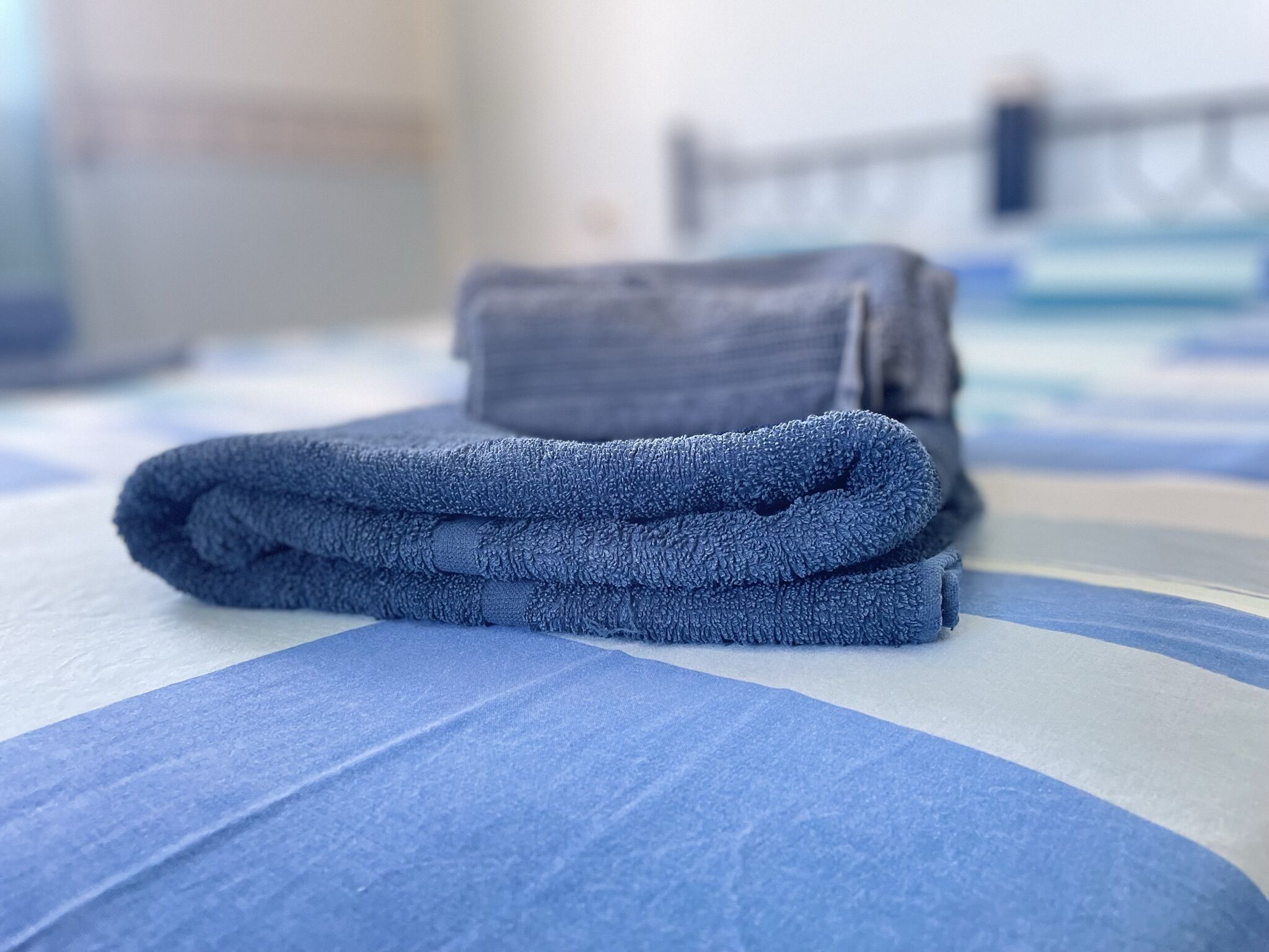 A neatly folded blue towel on a bed with a blue and white striped bedspread.