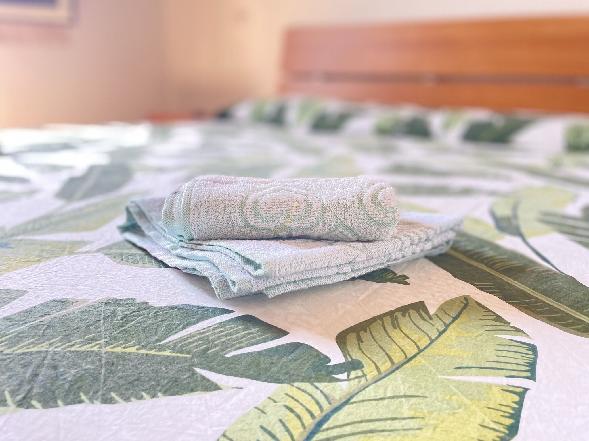 A bed with a floral-patterned bedspread and a folded towel on it.