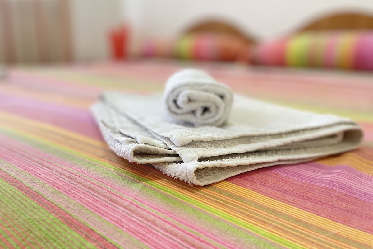A neatly folded towel on a striped bedspread in a hotel room.