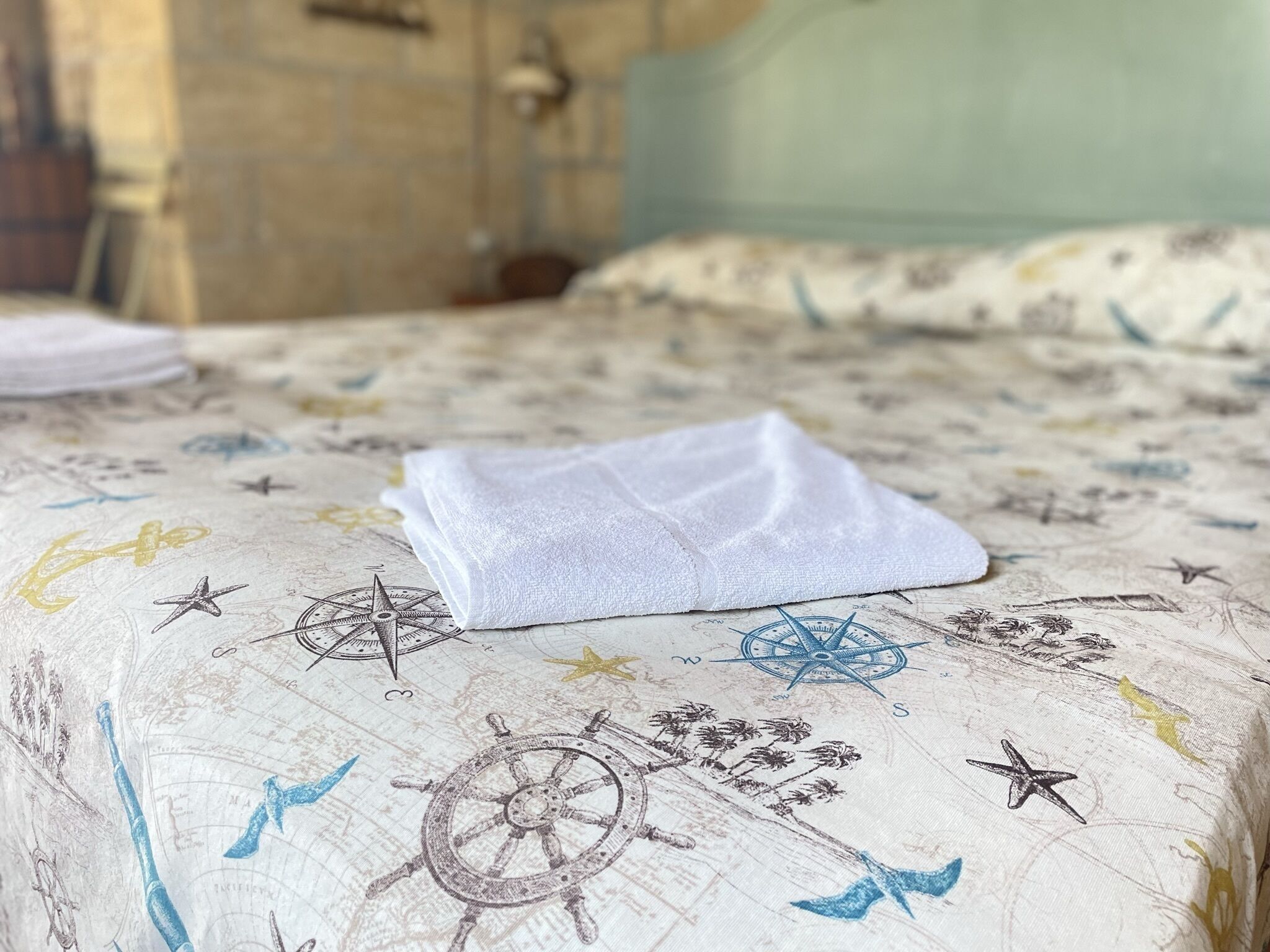 A bed with a nautical-themed bedspread, a folded white towel, and a visible headboard.