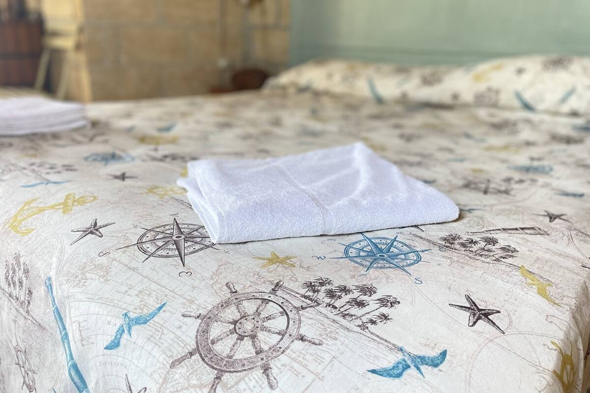 A bed with a nautical-themed bedspread, a folded white towel, and a visible headboard.