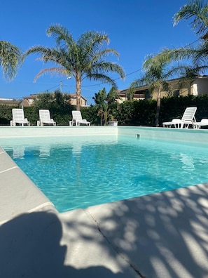A clear blue pool with white lounge chairs and palm trees. - Verter Home B&B (Isola di Capo Rizzuto)