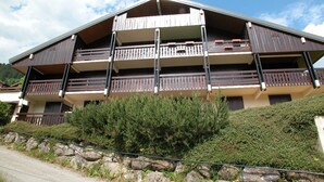 A multi-story building with balconies, a stone retaining wall, and a clear sky.