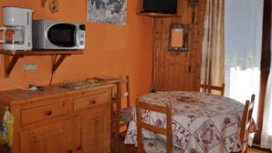A room with a wooden table, chairs, a microwave, a coffee maker, and a television mounted on the wall.