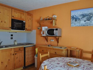 Cozinha compacta com armários de madeira, micro-ondas, fogão e pequena área de refeições com mesa e cadeiras.