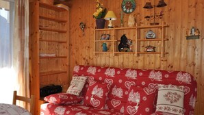 A cozy room with a wooden wall, a red patterned sofa, and shelves with various decorative items.