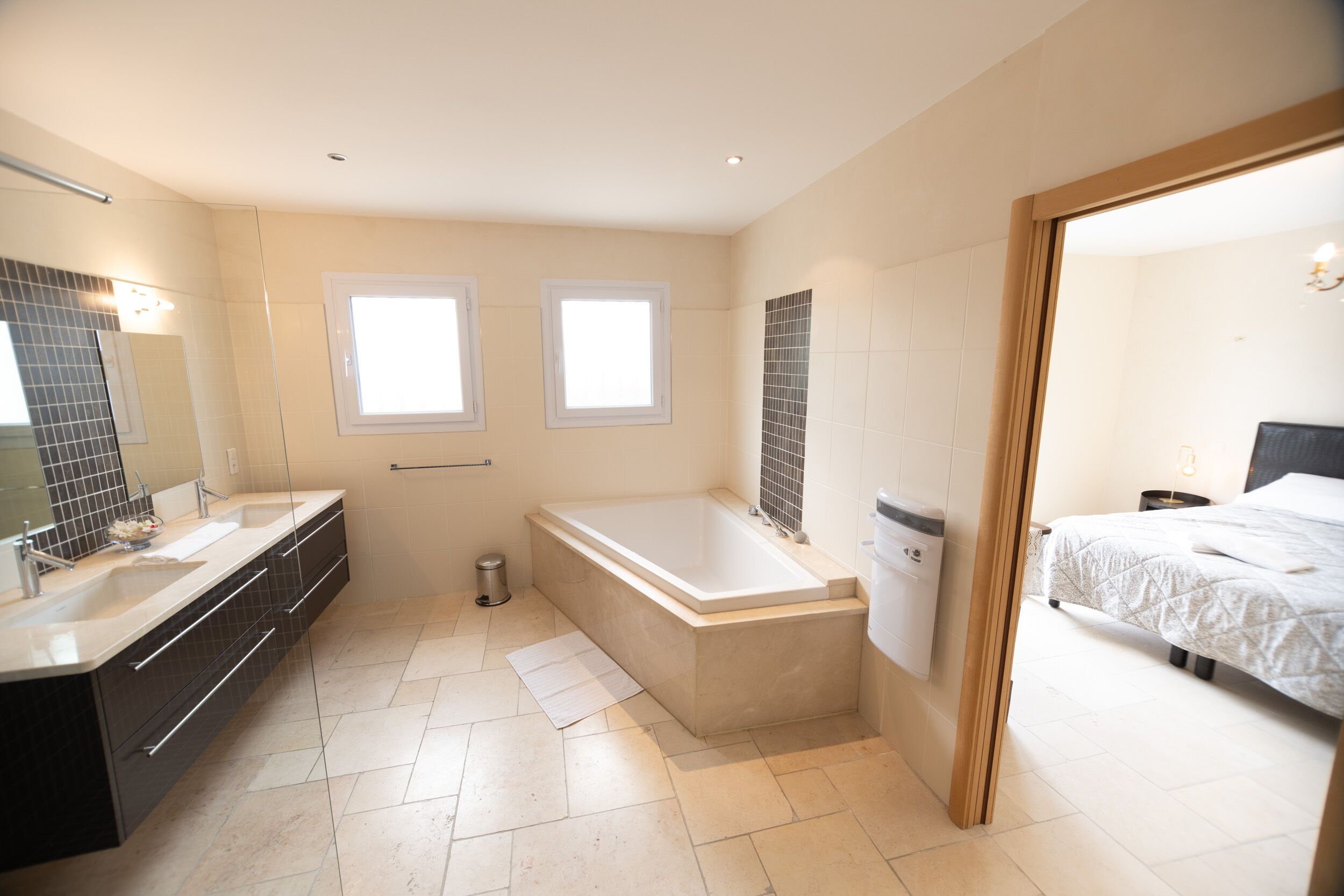 A modern bathroom with a bathtub, a large mirror, and a double sink.