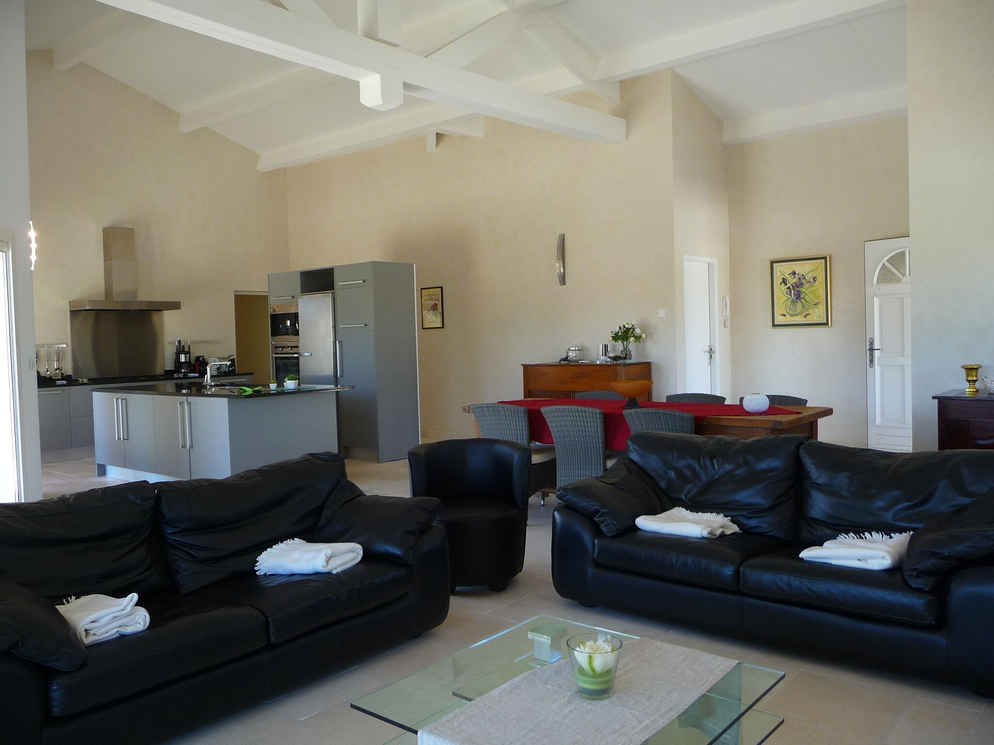 A spacious living area with two black leather sofas, a glass coffee table, and a kitchen in the background.