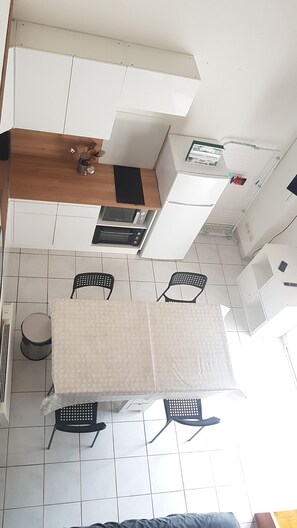 A kitchen with white cabinets, a wooden countertop, a microwave, and a stove. There are two black chairs and a table with a white tablecloth. - House 5 minutes from the beach, shared swimming pool in the residence (Narbonne)