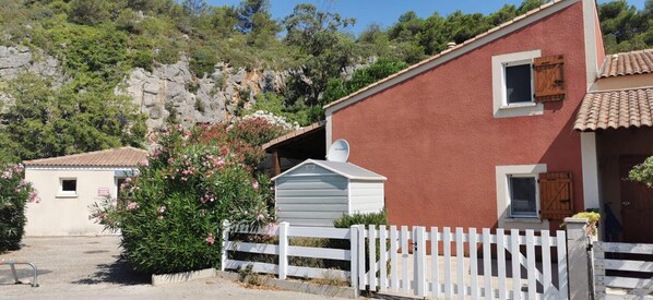 A red building with a white fence, a small shed, and a garden with pink flowers. - House 5 minutes from the beach, shared swimming pool in the residence (Narbonne)