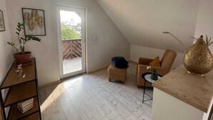 A spacious room with a high ceiling, a sliding glass door leading to a balcony, a sofa, a small table, and a decorative vase. - Cozy DG vacation apartment with balcony for 1 - 5 persons (Neustadt bei Coburg)
