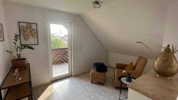 Ein geräumiger Raum mit hoher Decke, einer Schiebetür zum Balkon, einem Sofa, einem kleinen Tisch und einer dekorativen Vase.
